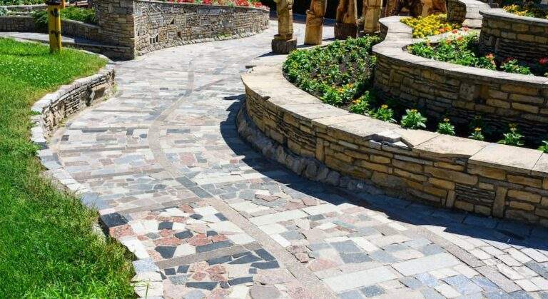 Curved mosaic stone garden path lined with multi-tiered natural stone retaining walls and flower beds.